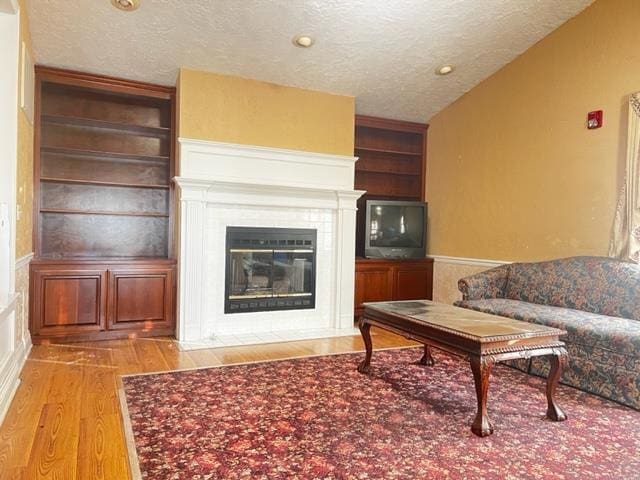 living room with a textured ceiling, built in features, and hardwood / wood-style floors