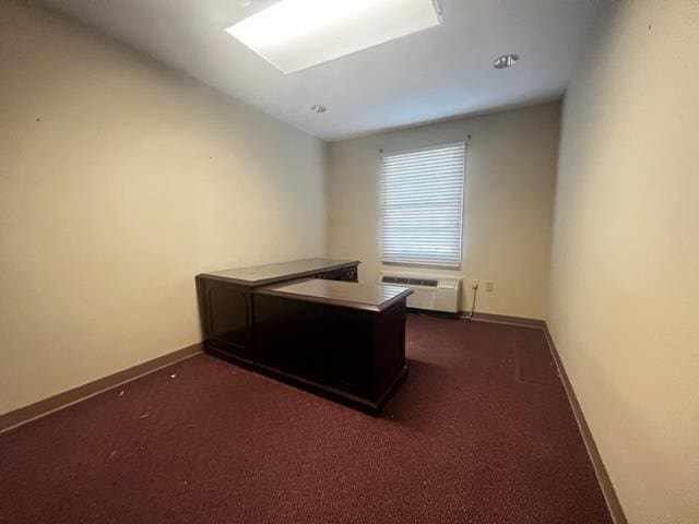office area featuring dark carpet, baseboards, and a wall unit AC