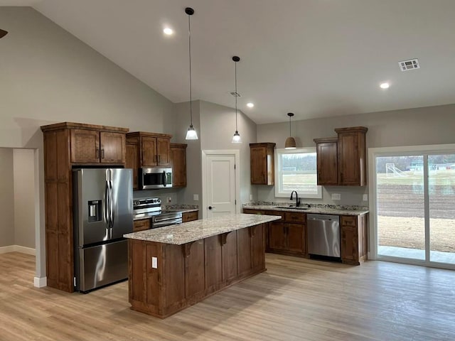 kitchen featuring sink, hanging light fixtures, light stone counters, a kitchen island, and appliances with stainless steel finishes