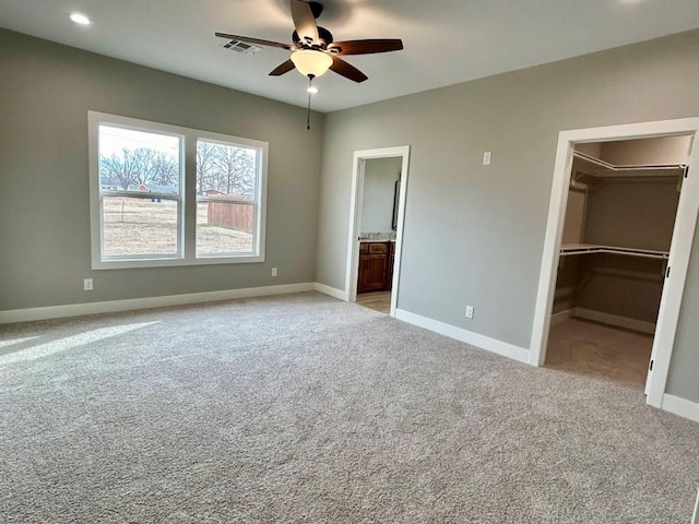 unfurnished bedroom featuring light carpet, ensuite bathroom, ceiling fan, a spacious closet, and a closet