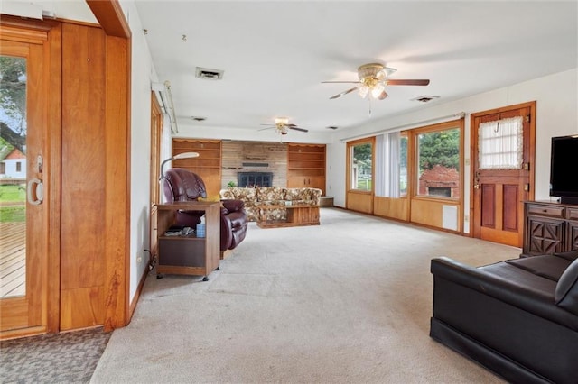 carpeted living room with wooden walls, ceiling fan, and a fireplace