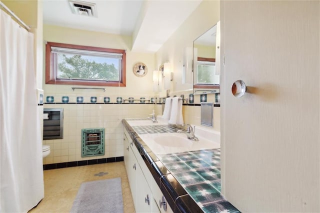 bathroom featuring tile patterned flooring, tile walls, heating unit, vanity, and toilet