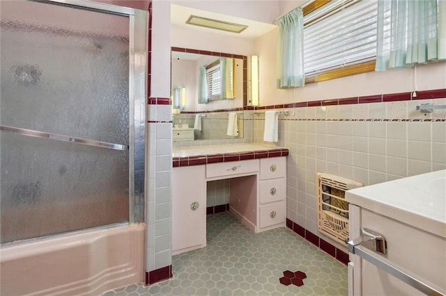 bathroom featuring bath / shower combo with glass door, a wealth of natural light, heating unit, tile walls, and vanity