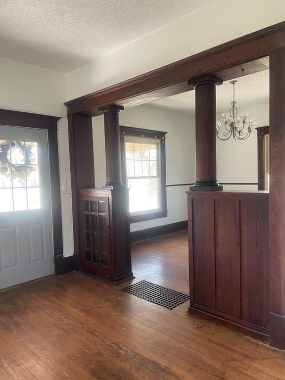 entryway with a textured ceiling, an inviting chandelier, ornate columns, and dark wood-type flooring