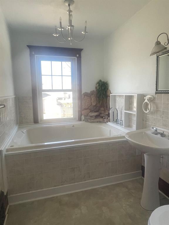 bathroom with a relaxing tiled tub, a notable chandelier, and sink