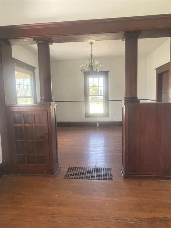 unfurnished dining area featuring dark hardwood / wood-style flooring, ornate columns, and a chandelier