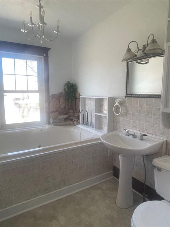 bathroom featuring a notable chandelier, toilet, and tiled tub