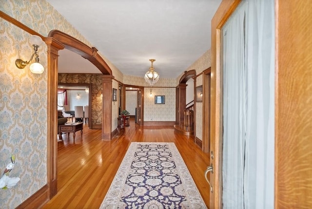 hallway featuring an inviting chandelier, light wood-type flooring, and ornate columns