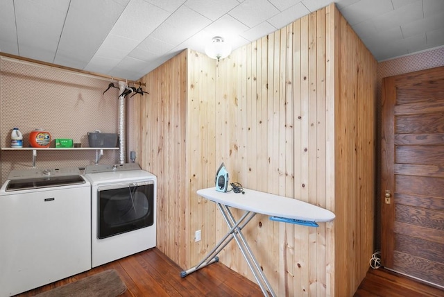 clothes washing area with wooden walls, washing machine and clothes dryer, and dark hardwood / wood-style flooring