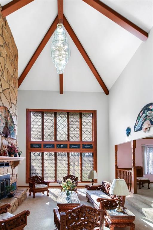 living room with an inviting chandelier, carpet, a stone fireplace, beam ceiling, and high vaulted ceiling