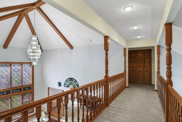 hall featuring carpet floors, a textured ceiling, a notable chandelier, and vaulted ceiling with beams