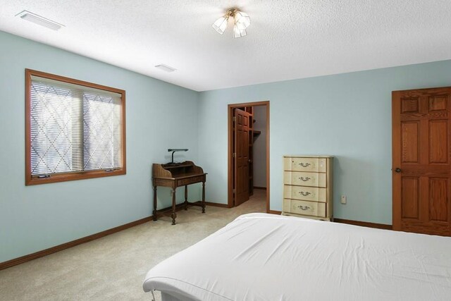 carpeted bedroom with a walk in closet, a closet, and a textured ceiling