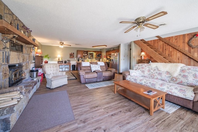 living room with a stone fireplace, hardwood / wood-style flooring, ceiling fan, and a textured ceiling