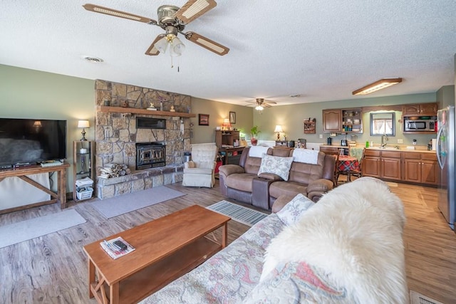 living room with light hardwood / wood-style floors, a textured ceiling, a fireplace, sink, and ceiling fan