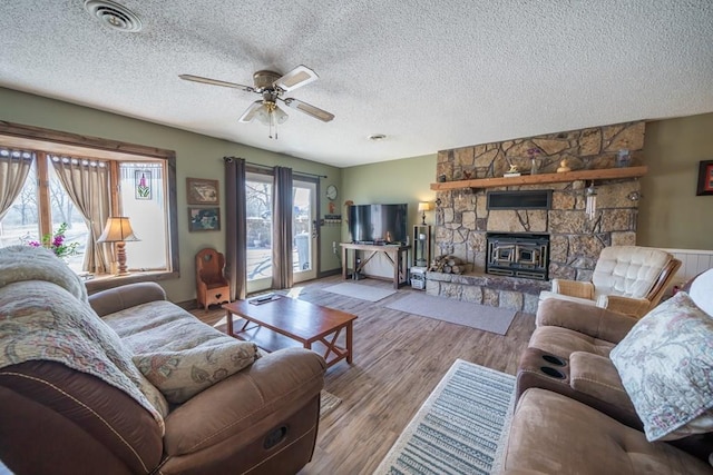 living room with a stone fireplace, a healthy amount of sunlight, ceiling fan, and hardwood / wood-style floors