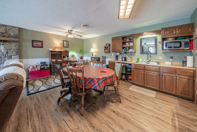 dining area with ceiling fan, sink, a textured ceiling, and light wood-type flooring