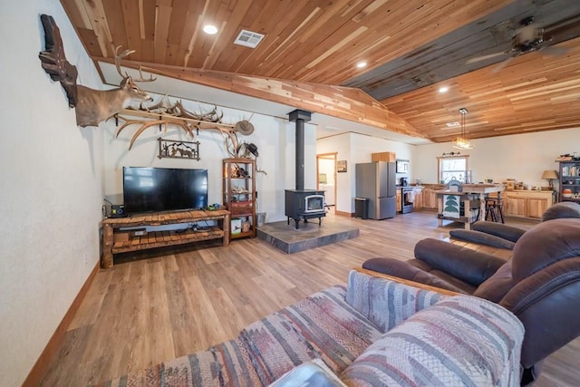 living room featuring vaulted ceiling, a wood stove, wood ceiling, and light hardwood / wood-style flooring