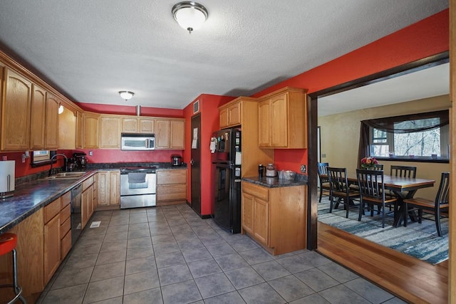 kitchen featuring tile patterned floors, a textured ceiling, sink, black appliances, and dark stone countertops