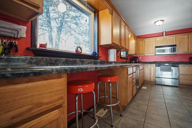 kitchen featuring a kitchen bar, stove, dark stone counters, and dark tile patterned flooring