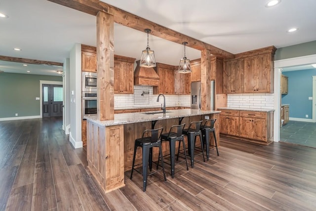 kitchen with custom range hood, decorative light fixtures, appliances with stainless steel finishes, sink, and a kitchen bar