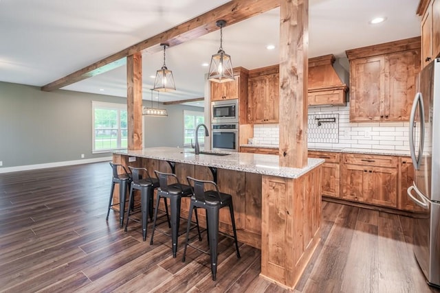 kitchen featuring a kitchen island with sink, pendant lighting, light stone counters, decorative backsplash, and appliances with stainless steel finishes