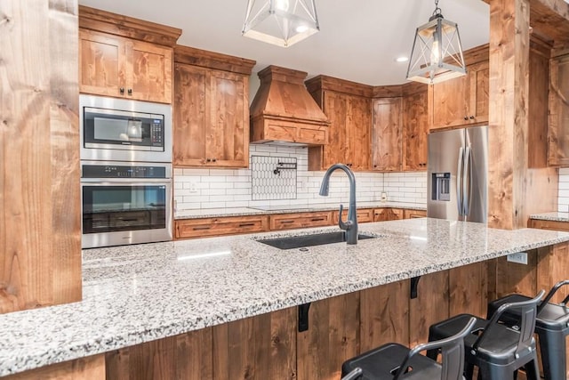 kitchen featuring a breakfast bar area, custom range hood, appliances with stainless steel finishes, sink, and light stone counters