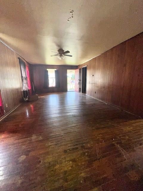 unfurnished room featuring a textured ceiling, ceiling fan, wood walls, and dark hardwood / wood-style floors