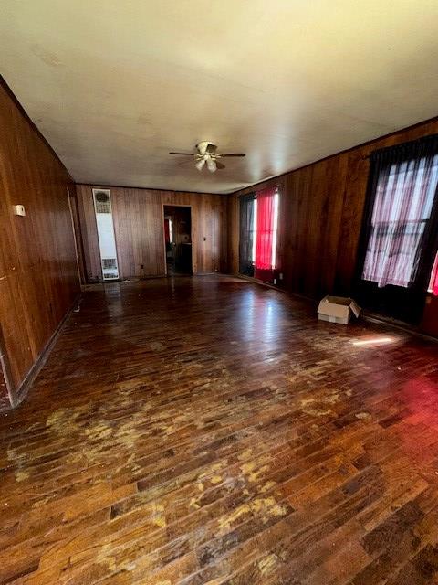 unfurnished living room featuring ceiling fan, wooden walls, and dark wood-type flooring