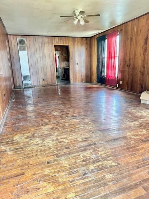 unfurnished living room featuring ceiling fan, dark wood-type flooring, and wood walls