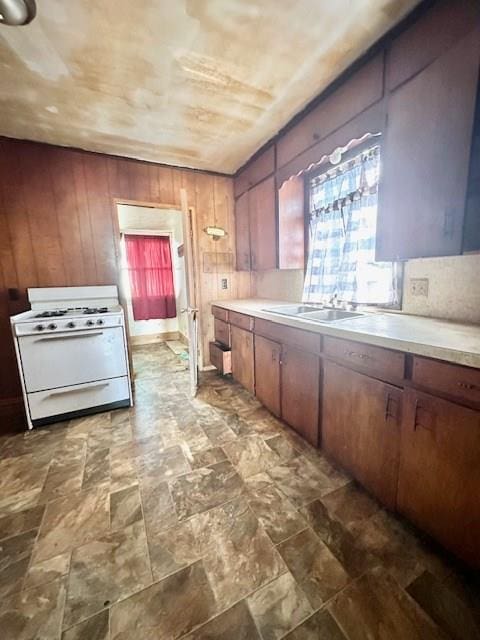 kitchen featuring white gas range, wooden walls, and sink