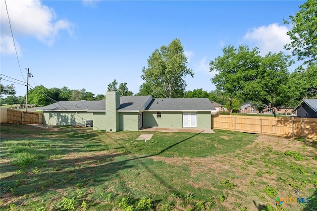 back of house with a fenced backyard, a patio, a chimney, and a lawn