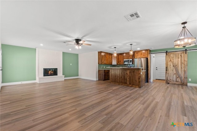 kitchen with a barn door, a ceiling fan, stainless steel microwave, open floor plan, and visible vents