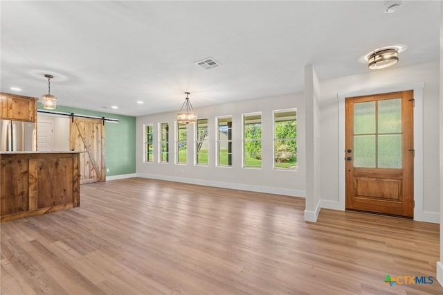 unfurnished living room featuring visible vents, a barn door, baseboards, light wood-style floors, and recessed lighting