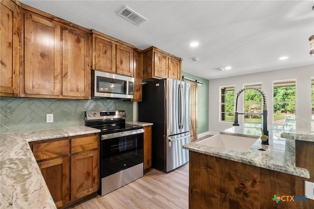 kitchen featuring appliances with stainless steel finishes, light wood-style floors, brown cabinetry, tasteful backsplash, and visible vents
