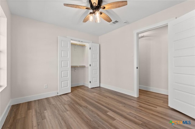 unfurnished bedroom featuring ceiling fan, baseboards, wood finished floors, visible vents, and a closet
