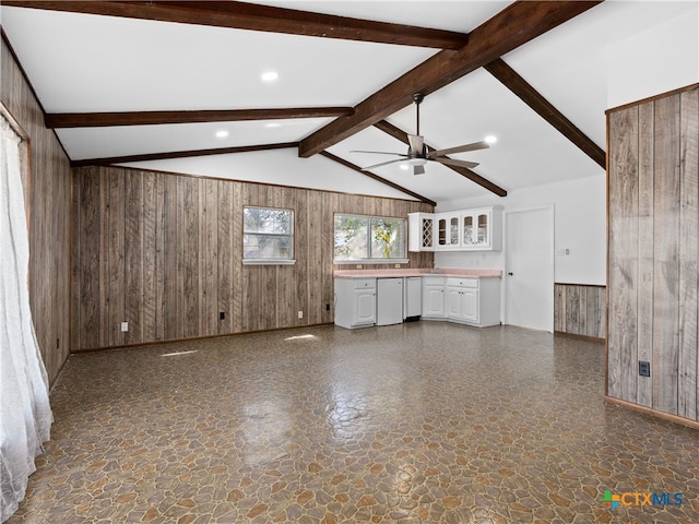 unfurnished living room featuring a ceiling fan, stone finish floor, vaulted ceiling with beams, and wooden walls