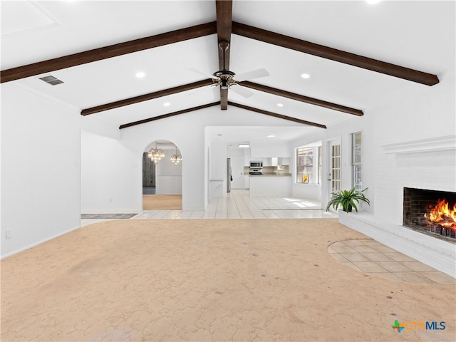 unfurnished living room featuring light carpet, visible vents, vaulted ceiling with beams, a brick fireplace, and ceiling fan with notable chandelier