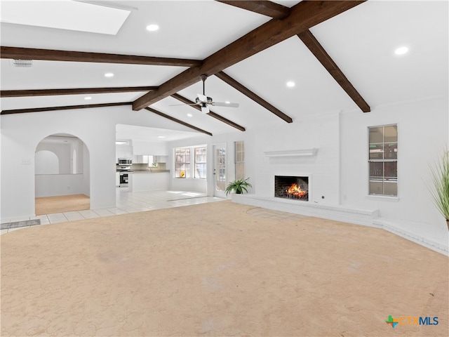 unfurnished living room featuring lofted ceiling with beams, ceiling fan, carpet flooring, a brick fireplace, and tile patterned floors