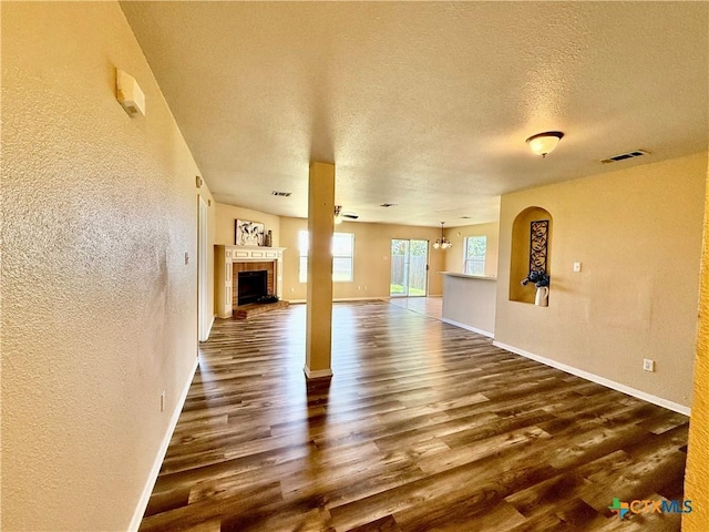 3807 Sunflower Dr, Killeen, TX 76542 - unfurnished living room with a textured wall, dark wood-style flooring, a brick fireplace, and a textured ceiling