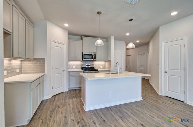 2588 Gideon Ln, New Braunfels, TX 78130 - kitchen featuring appliances with stainless steel finishes, light wood-type flooring, tasteful backsplash, light countertops, and an island with sink