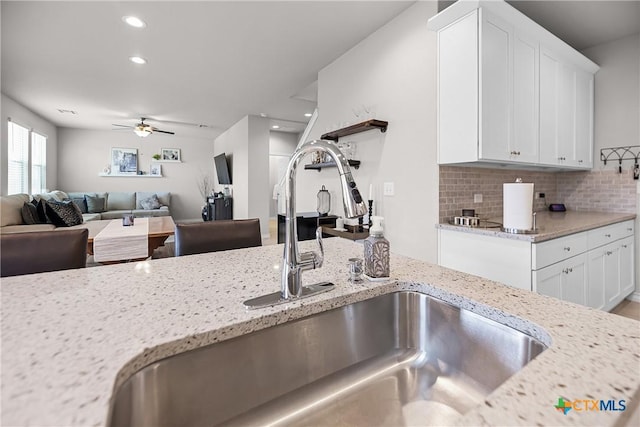 kitchen with ceiling fan, white cabinetry, backsplash, and a sink