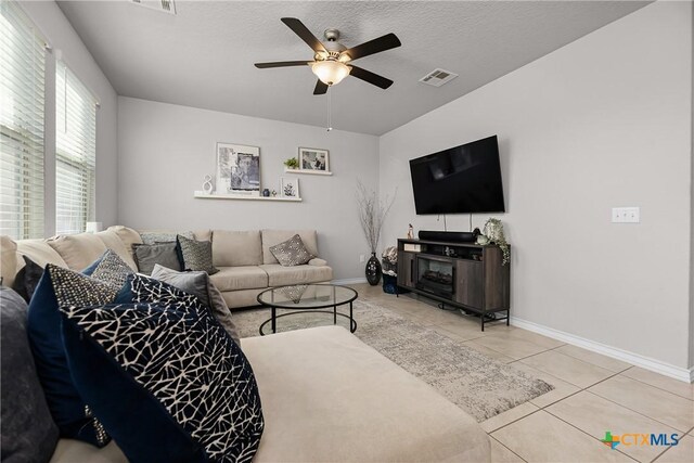 living room with tile patterned floors, visible vents, baseboards, and a ceiling fan