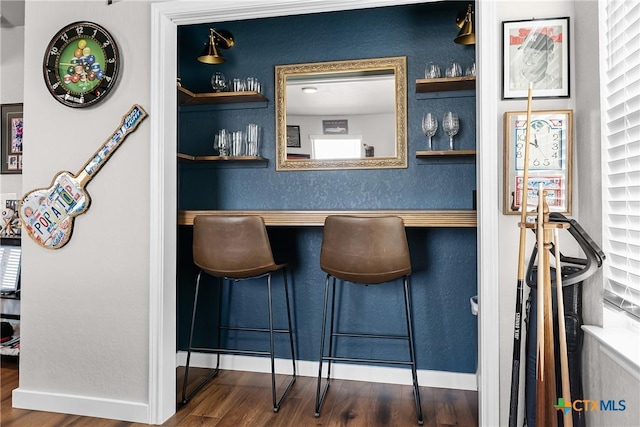 bar with baseboards, a bar, and wood finished floors