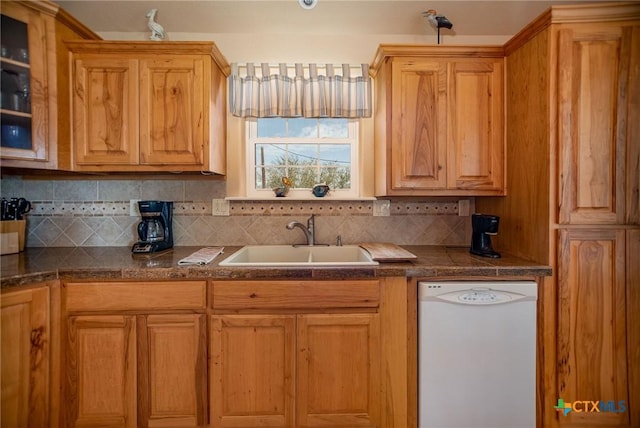 kitchen featuring decorative backsplash, dark countertops, glass insert cabinets, white dishwasher, and a sink