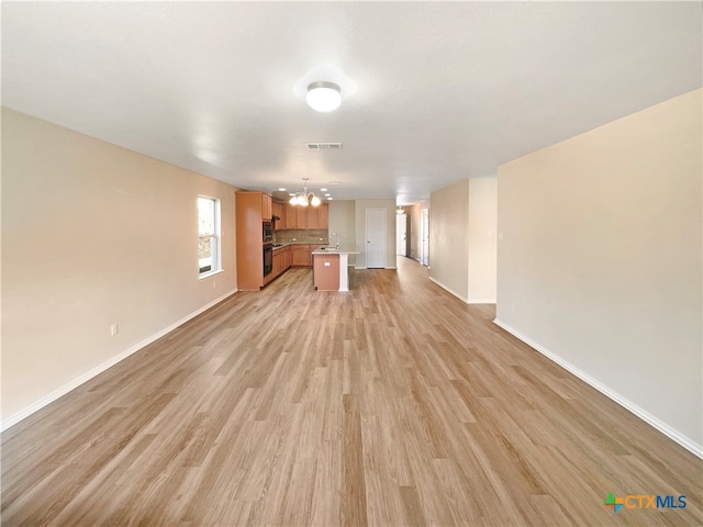 unfurnished living room featuring light hardwood / wood-style floors, a notable chandelier, and sink