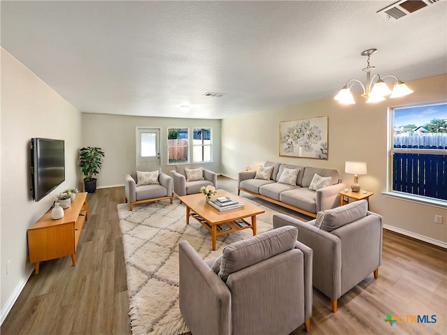 living room with light hardwood / wood-style flooring, a textured ceiling, and an inviting chandelier