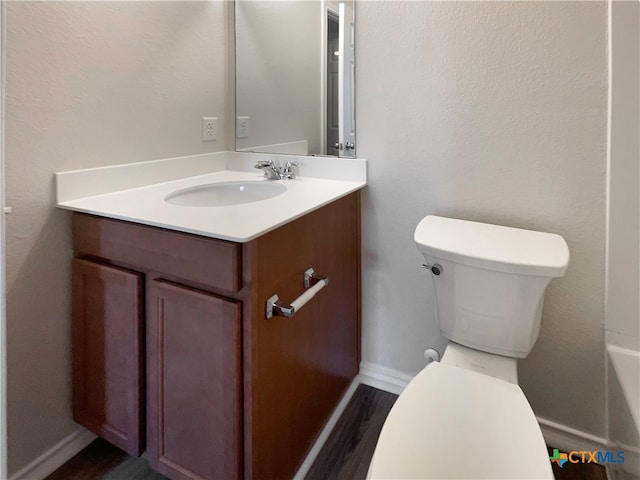 bathroom with hardwood / wood-style flooring, vanity, toilet, and a tub