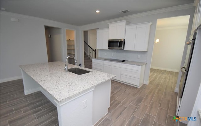 kitchen with white cabinetry, sink, light stone countertops, crown molding, and an island with sink