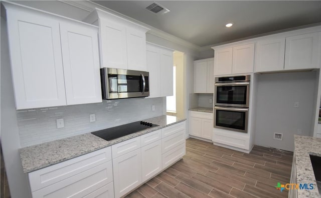 kitchen with decorative backsplash, stainless steel appliances, white cabinetry, and light stone countertops