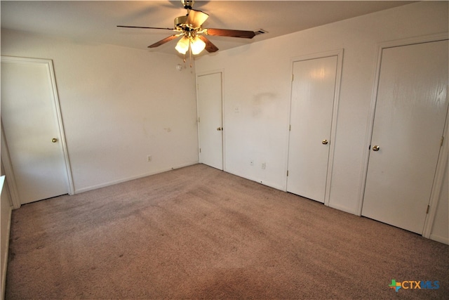 unfurnished bedroom featuring ceiling fan, light carpet, and two closets